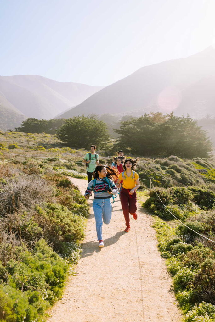group of diverse young adults running on a trail along the coast